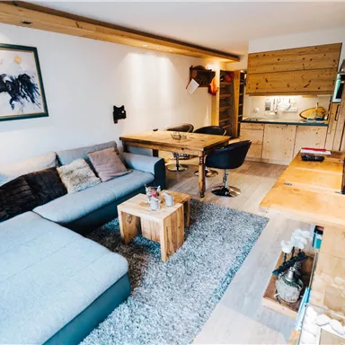 A modern living room with a large sofa and a wooden table. A piece of art featuring a horse hangs on the wall.