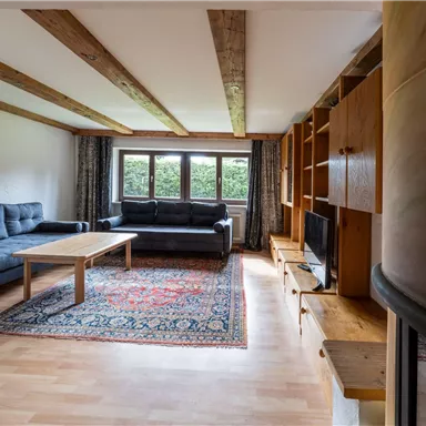 A cozy living room with two dark blue sofas and a wooden table. Large windows allow ample daylight in and create a bright atmosphere.