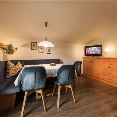 A cozy living space with a seating area and a dining table. The room is bright and cheerful, featuring a television and a dresser.