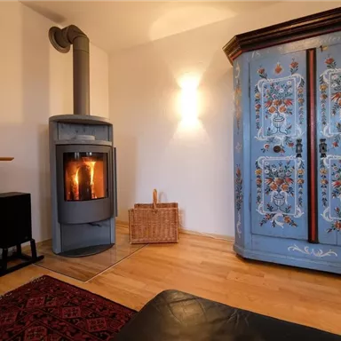 Ein gemütlicher Wohnraum mit einem modernen Kamin und einem bunten Schrank. Der Boden ist aus Holz und ein Teppich sorgt für zusätzliche Wärme.