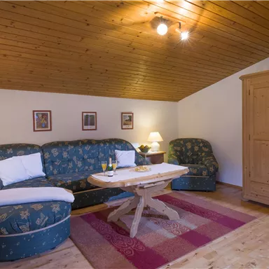 Ein gemütlicher Wohnraum mit einer blauen Couch und einem Holztisch. Die warmen Holzwände und die sanfte Beleuchtung schaffen eine einladende Atmosphäre.