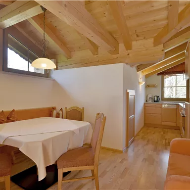 Ein gemütlicher Wohnbereich mit Holzbalken und einer kleinen Küche. Der Tisch ist für vier Personen vorbereitet.