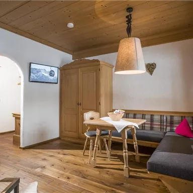 Ein gemütlicher Wohnraum mit Holzmöbeln und einem Esstisch. Die Wände sind hell, und es gibt ein großes Fenster mit einem schönen Blick.