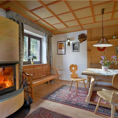 A cozy dining area with wooden paneling and an open fireplace. A table with chairs and fresh flowers create an inviting atmosphere.