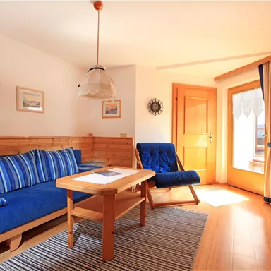 A cozy living room with blue furniture and wooden elements. There is a bright atmosphere and access to the balcony.