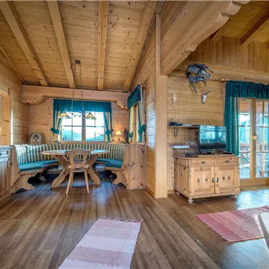 Eine gemütliche Holzwohnung mit einem offenen Wohnbereich. Die Einrichtung ist rustikal und einladend, mit einer Essgruppe und großen Fenstern.