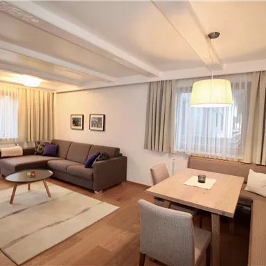 A modern living room with a comfortable couch and a dining table. Large windows provide plenty of daylight.