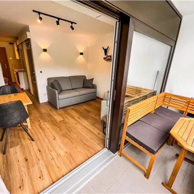 Ein gemütlicher Wohnbereich mit einem grauen Sofa und hellem Holzboden. Auf dem Balkon befindet sich eine Sitzgruppe aus Holz.