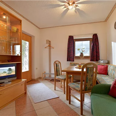 A cozy living space with a dining table, chairs, and a couch. The room is bright and friendly, with a window that lets in a lot of light.