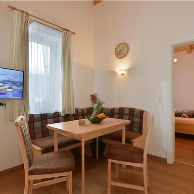 Ein gemütlicher Essbereich mit einem Tisch und Stühlen, ausgestattet mit einem Fernseher. Im Hintergrund ist ein Schlafzimmer sichtbar.