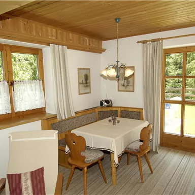 Ein gemütliches Esszimmer mit Holzverkleidung und einem Tisch. Große Fenster bieten einen Blick nach draußen in die Natur.