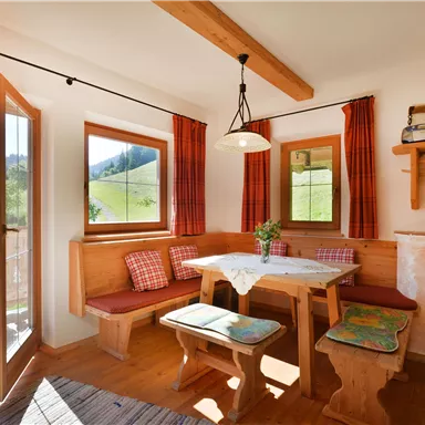 Ein einladendes Wohnzimmer mit Holzverkleidung und einem gemütlichen Essbereich. Große Fenster lassen viel Tageslicht herein und bieten einen Blick ins Grüne.