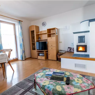 A cozy living space with a wood stove and a dining table. Bright colors and natural light sources create an inviting atmosphere.