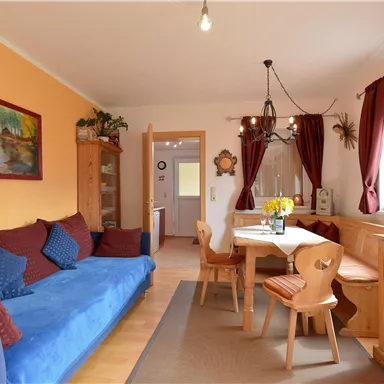 Ein gemütliches Wohnzimmer mit einem blauen Sofa, einem Holztisch und Stühlen. Die Wände sind orange und rot, und es gibt eine gute Beleuchtung.