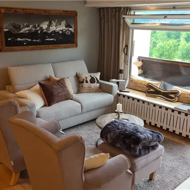 A cozy living room with a bright sofa and comfortable armchairs. Large windows offer a view of the greenery.