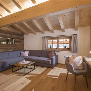 A modern living space with a comfortable gray sofa and a wooden chair. Large windows provide plenty of daylight and a warm atmosphere.