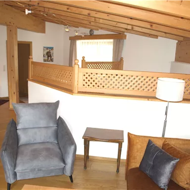 Ein gemütliches Wohnzimmer mit Holzdecken und modernen Möbeln. Es gibt einen blauen Sessel und eine braune Couch im Raum.