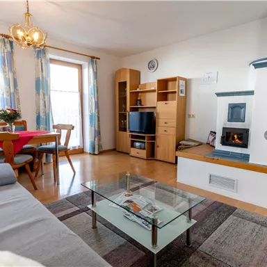 A cozy living space with a sofa, a glass table, and a modern fireplace. The room is bright and inviting, with a dining area and windows that let in plenty of light.