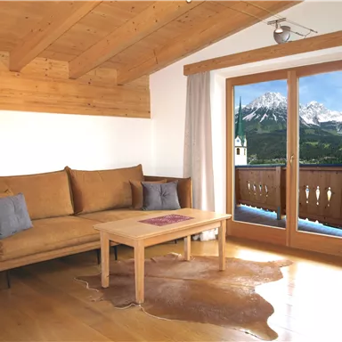 Ein gemütliches Wohnzimmer mit einem Sofa und einem Holztisch. Große Fenster bieten einen wunderschönen Blick auf die Berge.