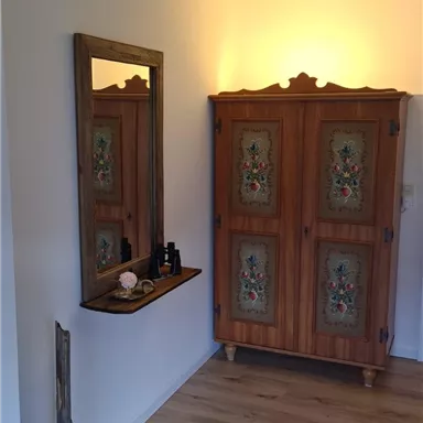 A cozy room with a decorative cabinet and a mirror on the wall. The light wooden floor complements the warm atmosphere.