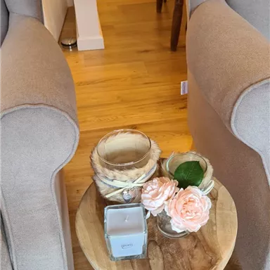Two comfortable armchairs are next to a small wooden table. On the table, there is a candle, artificial flowers, and a small container placed.