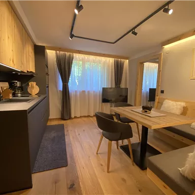 Eine moderne Küche mit einem Essbereich und gemütlicher Sitzgelegenheit. Das Zimmer ist hell und freundlich, mit Holz- und Grautönen eingerichtet.