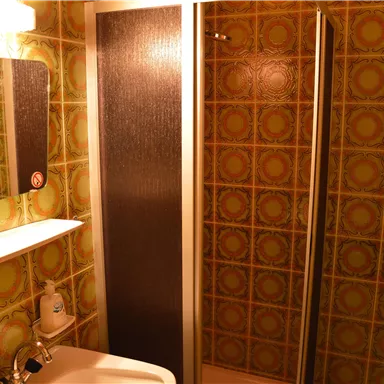 Ein kleines Badezimmer mit einer Dusche und einem Waschbecken. Die Wände sind mit einem grünen, gemusterten Fliesenstil dekoriert.