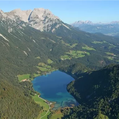 A breathtaking mountain landscape with high peaks and a clear lake in the center. Green meadows and forests surround the scene.