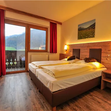 Ein gemütliches Hotelzimmer mit zwei Betten und warmen Holzdetails. Große Fenster bieten einen schönen Blick auf die Landschaft.