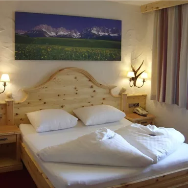 Ein gemütliches Schlafzimmer mit einem großen Holzbett und dekorativen Kissen. An den Wänden hängen Bilder und es gibt sanfte Beleuchtung von Wandlampen.
