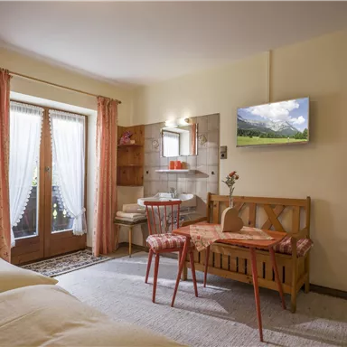 Ein gemütliches Zimmer mit zwei Betten, einem Tisch und Stühlen. Große Fenster sorgen für viel Tageslicht und Blick ins Freie.