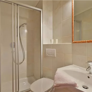 A modern bathroom with a shower cabin and a sink. The walls are brightly tiled and the room is neatly furnished.