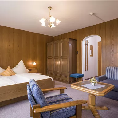 A cozy hotel room with wooden walls. It features a double bed, a seating area, and a table.