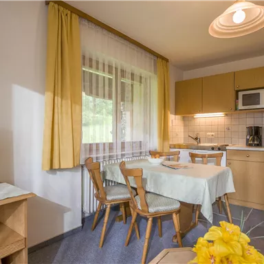 A cozy room with a small kitchen, a dining table, and a television. The large windows provide plenty of daylight and an inviting atmosphere.