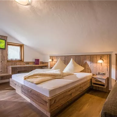 Ein gemütliches Schlafzimmer mit Holzverkleidung und einem großen Doppelbett. Es gibt einen kleinen Tisch und Fenster mit Blick ins Freie.