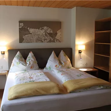 Ein gemütliches Schlafzimmer mit einem großen Doppelbett und dekorativen Kissen. An der Wand hängt ein Gemälde und die Einrichtung ist modern und freundlich.