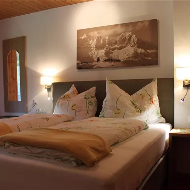 Ein gemütliches Schlafzimmer mit zwei Betten, flauschigen Kissen und Decken. Im Hintergrund hängt ein Bild an der Wand, und es gibt sanfte Beleuchtung.