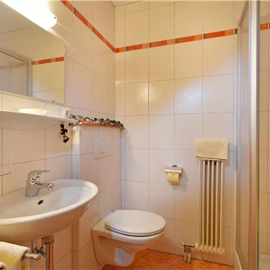 A modern bathroom with white tiles and orange accents. It includes a shower, a sink, and a toilet.