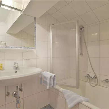 A modern bathroom with a bathtub and a shower. The walls are bright tiled, and there is a large mirror above the sink.