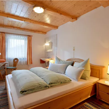 A cozy bedroom with a wooden ceiling and bright colors. There is a bed with quilted pillows and a small table with chairs.
