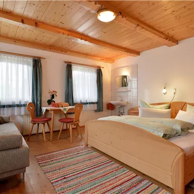 A bright room with wooden ceilings and furniture. There is a large bed, a seating area, and a small dining table.