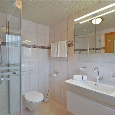 Ein modernes Badezimmer mit einer Dusche und einer Badewanne. Die Wände sind hell gefliest, und es gibt große Spiegel sowie Handtücher.