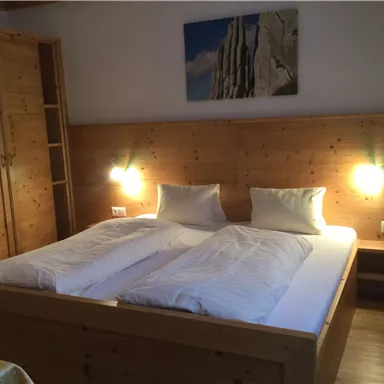 Ein gemütliches Zimmer mit einem großen Doppelbett und Holzverkleidung. An der Wand hängt ein Bild, und es gibt Nachttische mit integrierten Lampen.