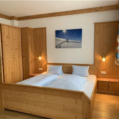 Ein gemütliches Schlafzimmer mit einem Doppelbett und hellem Holz. Die Wände sind dekoriert, und ein Bild von Skifahrern hängt über dem Bett.