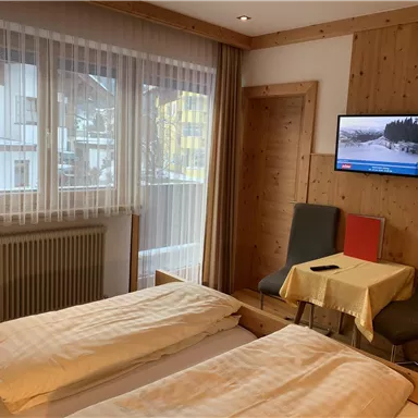 Ein gemütliches Hotelzimmer mit zwei Betten, einem Tisch und Stühlen. Es gibt ein Fenster mit Blick nach draußen und einen Fernseher an der Wand.