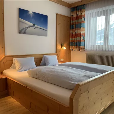 Ein gemütliches Schlafzimmer mit einem großen Holzbett und sanften Farben. An der Wand hängt ein Bild von Schnee und Bergen.