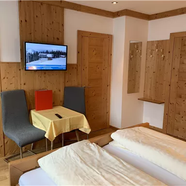 Ein gemütliches Hotelzimmer mit Holzwänden, einem Fernseher und einem kleinen Tisch. Das Zimmer verfügt über zwei Betten und eine einladende Atmosphäre.