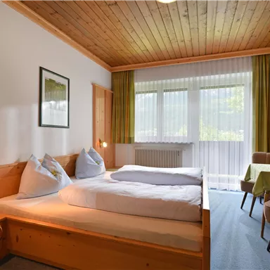 Ein gemütliches Zimmer mit Holzvertäfelung und zwei Einzelbetten. Große Fenster lassen viel natürliches Licht herein und bieten einen Blick auf die Natur.