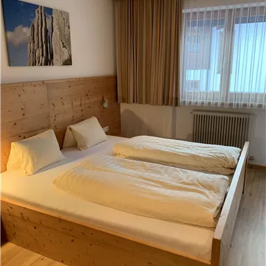 Ein gemütliches Schlafzimmer mit einem großen Doppelbett und Holzverkleidung. Das Zimmer hat ein Fenster mit Vorhängen und ein attraktives Wandbild.