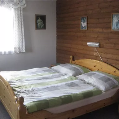 Ein gemütliches Schlafzimmer mit einem großen Holzbett und gestreifter Bettwäsche. Die Wände sind holzvertäfelt und es gibt ein Fenster mit Vorhängen.